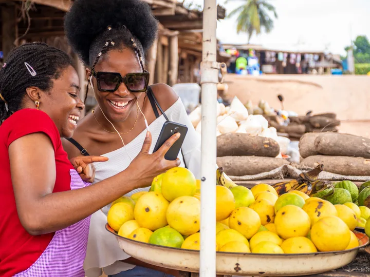 Deux commerçantes riant devant un téléphone à leur étal de fruits